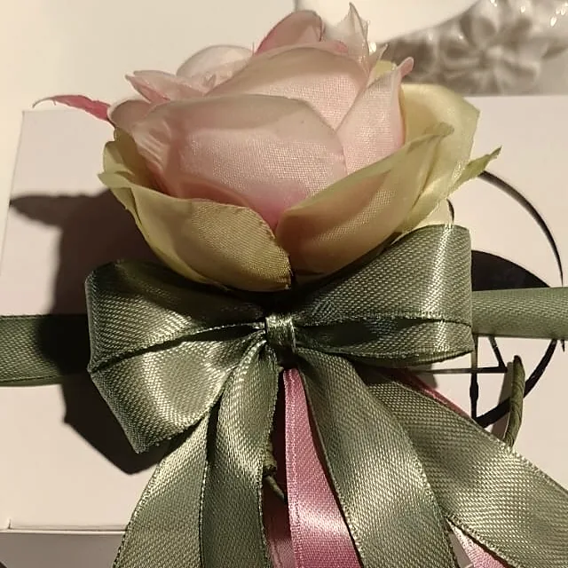 Dettaglio di una rosa tessile cipria su fiocco in raso salvia con nastro rosa